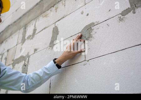 Asian engineer in uniform at construction site while checking and inspecting concrete material for house building. Professional engineering manager working on structure building at workplace. Stock Photo