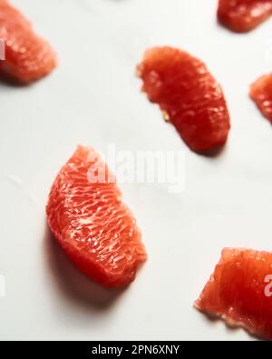 Peeled and sliced, divided in sections grapefruit on the white marble countertop. Bright, hey-key vertical photo. Stock Photo