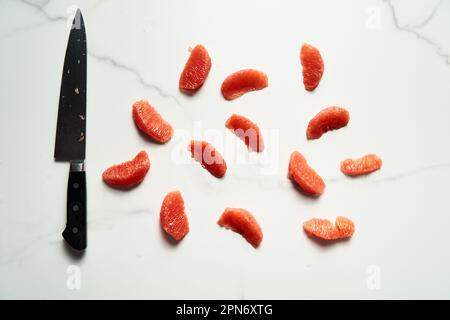 Peeled and sliced, divided in sections grapefruit with a knife next to it on the marble countertop. Top view food photo Stock Photo