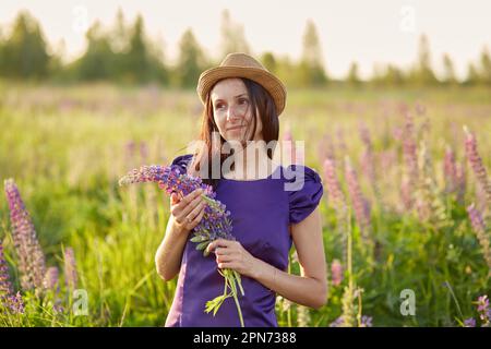 Wellness, mindful woman in summer field with lupins. Connecting with nature, well being, life balance concept. Stock Photo