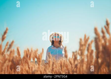 A young female wearing sunglasses standing in a field of golden wheat, enjoying the summer sun Stock Photo