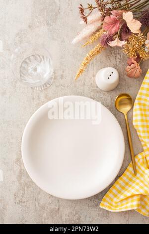 Table setting, plate and golden cutlery with yellow napkin on a brown background, empty wine glass and water glass Stock Photo