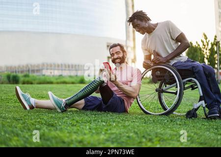 Multiracial friends with disability having fun using mobile phone at park city - Focus on man hand holding smartphone Stock Photo