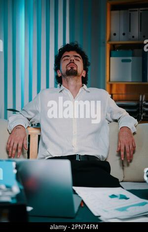 Tired exhausted businessman leaning back in his chair after working with documents all night long Stock Photo