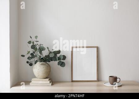 Boho breakfast still life. Cup of coffee, books. Empty wooden picture frame mockup on desk, table. Textured vase with silver eucalyptus leaves Stock Photo