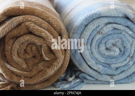 Woolen checkered plaid blanket isolated on a white background. Beige-brown and white-blue rolled blanket. Close up. Stock Photo