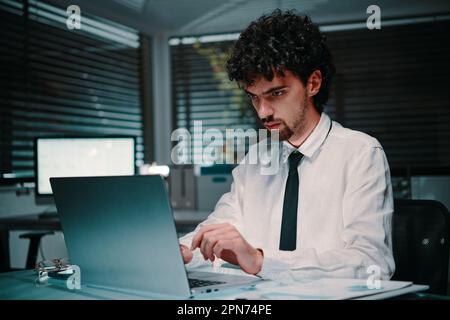 Portrait of serious young entrepreneur working on laptop late at nigh, workaholic concept Stock Photo