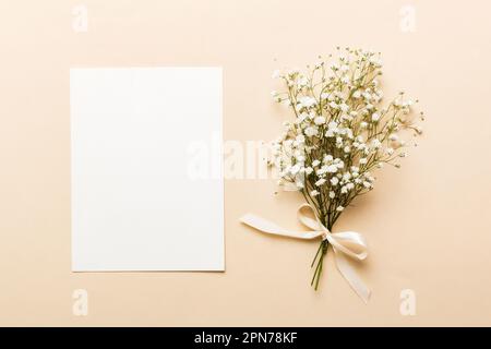 Wedding mockup with white paper list and flowers gypsophila on colored table top view flat lay. Blank greeting cards and envelopes. Beautiful floral p Stock Photo