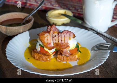 Eggs Benedict with bacon, toast bread and tomato, close up. Sandwich with poached egg for cooked breakfast Stock Photo