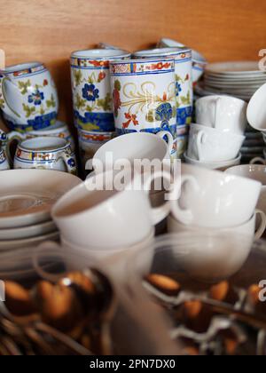 Various cups in a cupboard with tea spoons in the foreground Stock Photo