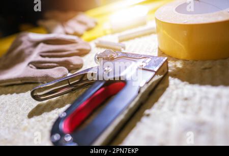 Closeup of Silver Industrial Staple Gun and Yellow Tape Lying in Bright Light on Construction Site. Contractor's Essential Working Tools. Stock Photo