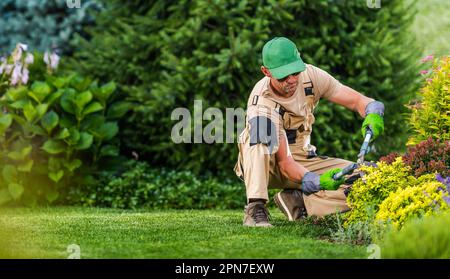Professional Caucasian Landscaper Performing Seasonal Garden Maintenance. Greenery Background with Copy Space on the Left. Stock Photo