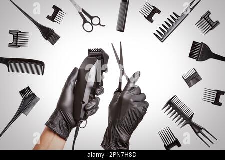 Hairdressers hands in black rubber gloves holds hair clipper and scissors surrounded by professional hairdressing accessories, close up Stock Photo