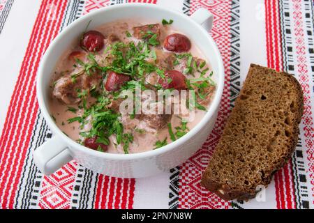 Delicious beef stew with cherries, black bread, in a white bowl, on an embroidered Ukrainian napkin. Stock Photo