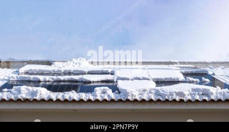 Solar Autonomous Photovoltaic Panel half covered with fluffy white snow on house tile rooftop. Ecological renewable electric energy source, profit. Stock Photo