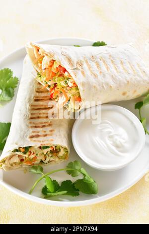 Tortilla wraps with chicken and fresh vegetables on plate over light background. Close up view Stock Photo