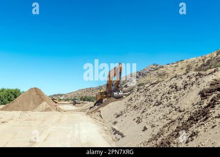 Boegoeberg Dam, South Africa - Feb 28 2023: Backhoe loaders clearing sand that blocked the irrigation canal from the Boegoeberg Dam Stock Photo