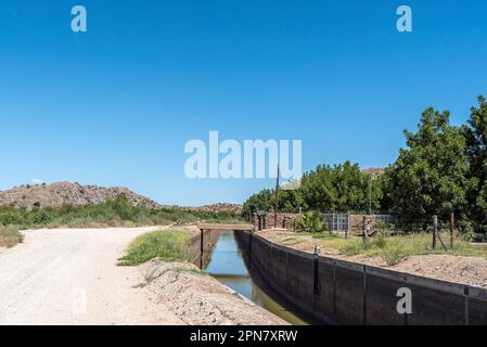 Boegoeberg Dam, South Africa - Feb 28 2023: The road and irrigation canal at Sandpunt farm between Brandboom and Boegoeberg Dam. A pecan plantation is Stock Photo