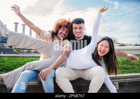 A group of young multiracial people having fun together. Three mixed teenagers smiling looking at camera. One asian woman spreading on top of her friends. Diverse students bonding on a social meeting. High quality photo Stock Photo