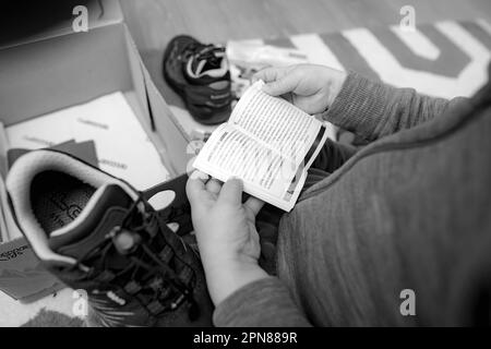 Frankfurt, Germany - Mar 12, 2023: A young child is seen indoors, holding an instruction manual while intently reading it. The stylish lowa boots stand nearby. Stock Photo