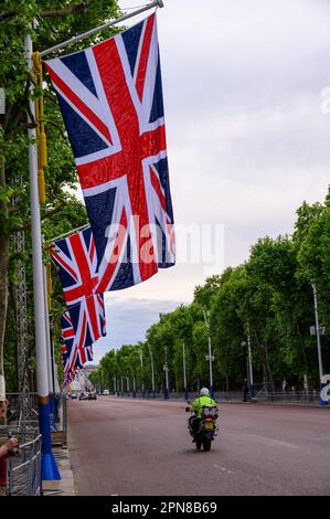 LONDON - May 18, 2022: Union Jack flags fly above The Mall, adding patriotic spirit to the Platinum Jubilee celebrations, as a motorcyclist passes by. Stock Photo