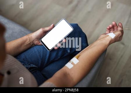 Closeup of unrecognizable man using smartphone with white screen mockup during IV drip treatment Stock Photo