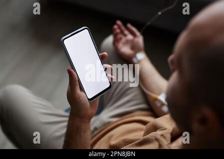 Closeup of adult man using smartphone with white screen mockup during IV drip treatment Stock Photo