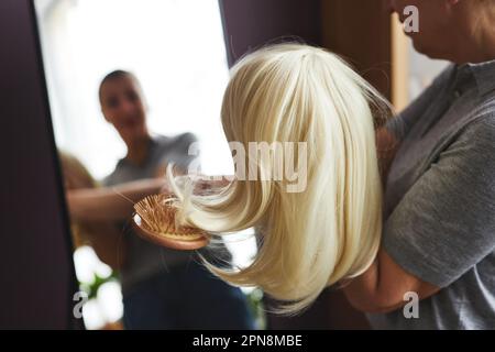 Closeup of unrecognizable woman brushing wig by mirror at home, copy space Stock Photo