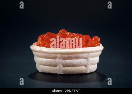 Tartlet with red caviar on a black background. Structure of caviar of a salmon, cold appetizers Stock Photo