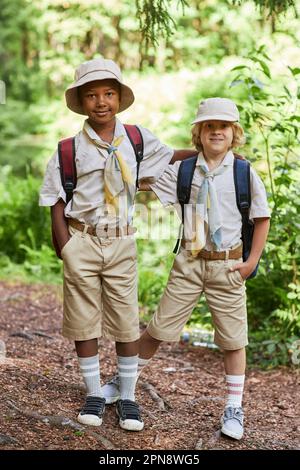 Vertical full length portrait of two cute boy scouts looking at camera outdoors in forest while enjoying field trip Stock Photo