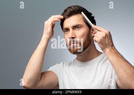 Beauty, grooming and hairstyle concept. Handsome caucasian bearded middle aged man brushing hair with comb Stock Photo