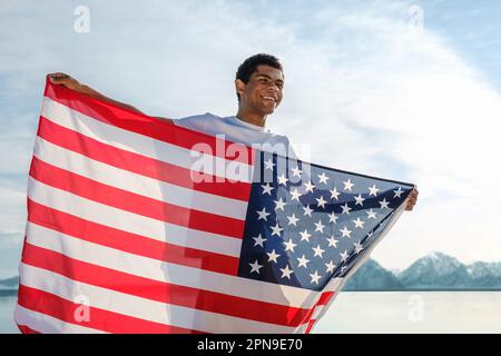 African-American man proudly holds an American flag against a blue sky Stock Photo