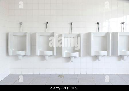 Row of white porcelain urinals and tiles  in a toilet in Portugal Stock Photo