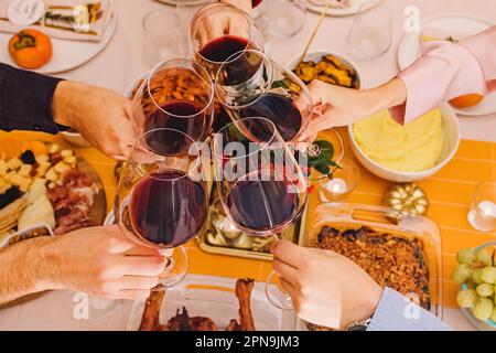 Hands clinking with a glasses filled with red wine at the Thanksgiving dinner table. Celebration, gather, Friendsgiving Stock Photo