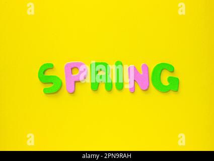 Colored letters spelling out spring on Yellow background with copy space. Greeting card with colored letters Spring on yellow backdrop. Stock Photo