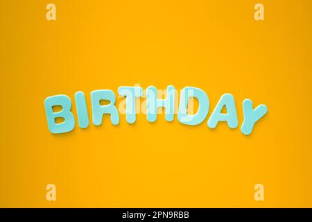 Top view of The text Birthday with blue letters on bright orange background with copy space. Happy Birthday concept or background Stock Photo