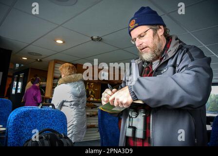 Alaskan man writing down bird observation notes during a wildlife and whale watching tour boat ride in Sitka, Alaska, USA. Stock Photo