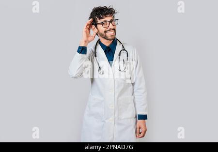Smiling doctor listening to a rumor. Young doctor smiling with hand over ear isolated, Smiling doctor extending hand isolated Stock Photo