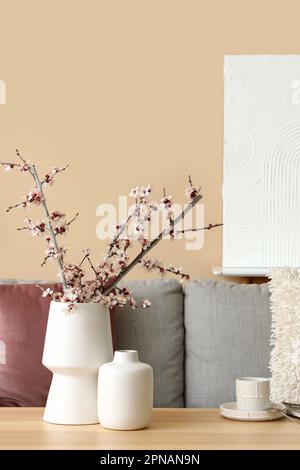 Vases with blooming branches and cup of coffee on table in living room Stock Photo