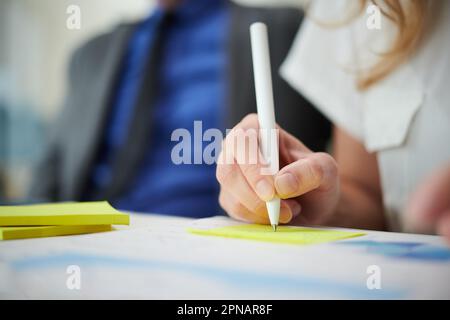 Closeup image of businesswoman taking notes on yellow stikers when working with financial documents Stock Photo