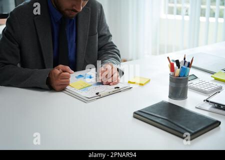 Serious entrepreneur analyzing chart and taking notes on yellow sticker Stock Photo