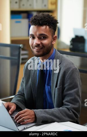 Portrait of positive businessman answering e-mails from business partners when working on laptop in office Stock Photo