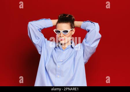 Portrait of playful adult woman in sunglasses holding hands behind head Stock Photo