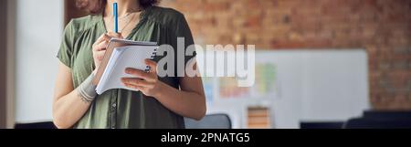 Cropped shot of woman, interior designer or architect in casual wear with messy hairdo holding notebook and making notes, working on creative project Stock Photo
