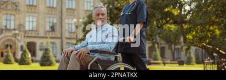 Full length shot of caring young nurse wearing face shield and mask walking with mature man patient in wheelchair Stock Photo