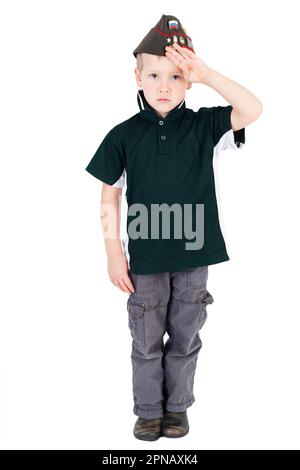 Young caucasian boy saluting playing dressups in green army shirt russian folding army hat - pilotka - from Soviet Red Army with pins. Creative play Stock Photo