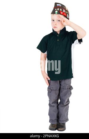 Young caucasian boy saluting in respect looking front on playing dressups in Russian folding army hat, pilotka, from Soviet Red Army Authority concept Stock Photo