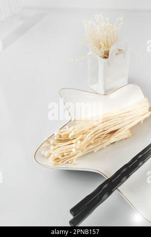 fresh enoki mushrooms or golden needle mushrooms on a star-shaped plate. Flammulina velutipes of the Physalacriaceae family is ready for cooking. Stock Photo