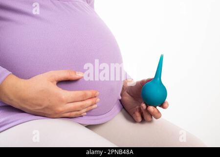 A pregnant girl in a purple blouse holds a syringe in her hand against the  background of her stomach. The concept of an enema in pregnant women during  Stock Photo