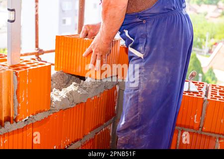 Spirit level for control measurement stuck in hollow of red ceramic block, mason bricklayer worker is using bricks to mount wall of building under con Stock Photo
